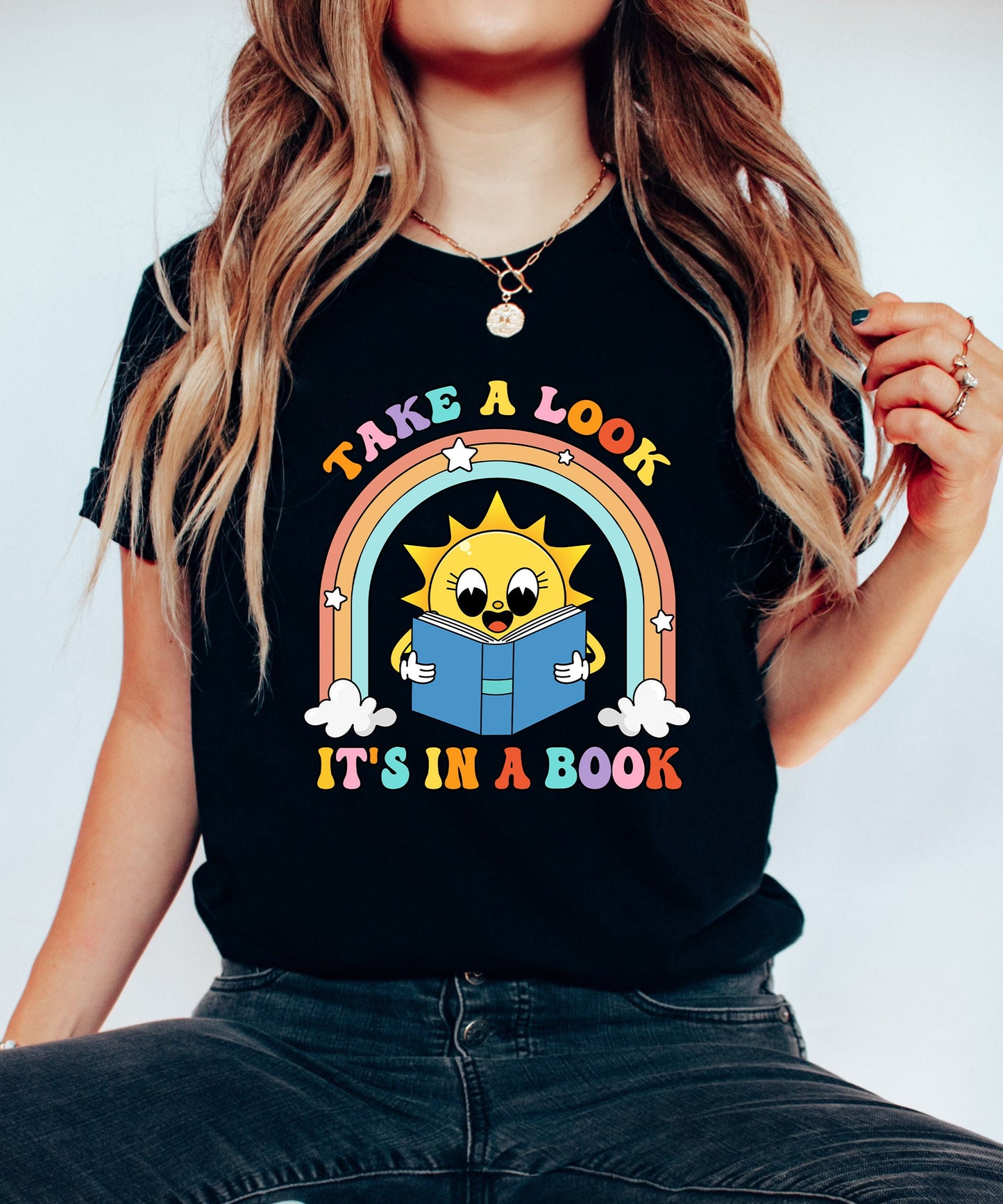 An uplifting design showcasing a sunny character engrossed in a book with a rainbow and stars surrounding it The text take a look it&#39;s in a book is prominently featured in colorful letters for a whimsical feel