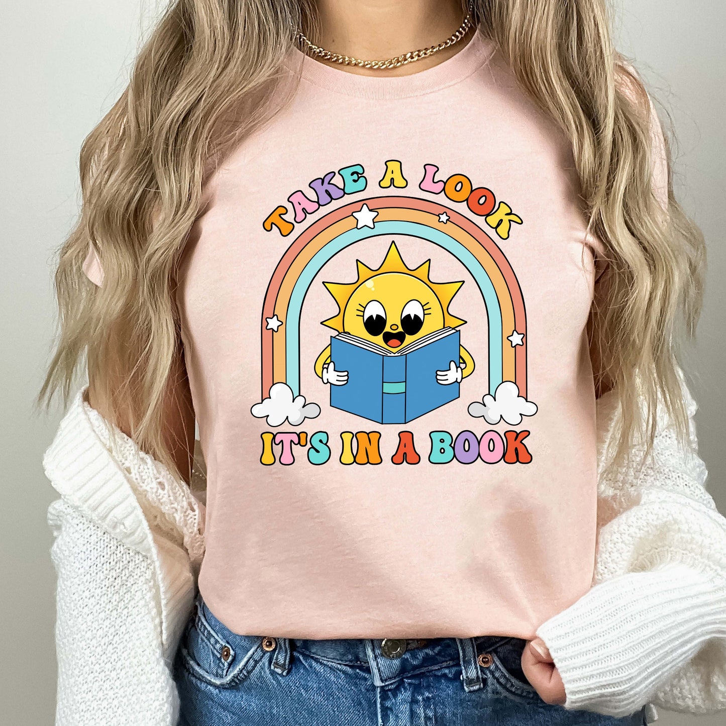 A fun and engaging design featuring a sun reading a book under a rainbow with fluffy clouds The phrase take a look it&#39;s in a book is displayed in vibrant letters capturing a sense of wonder and learning