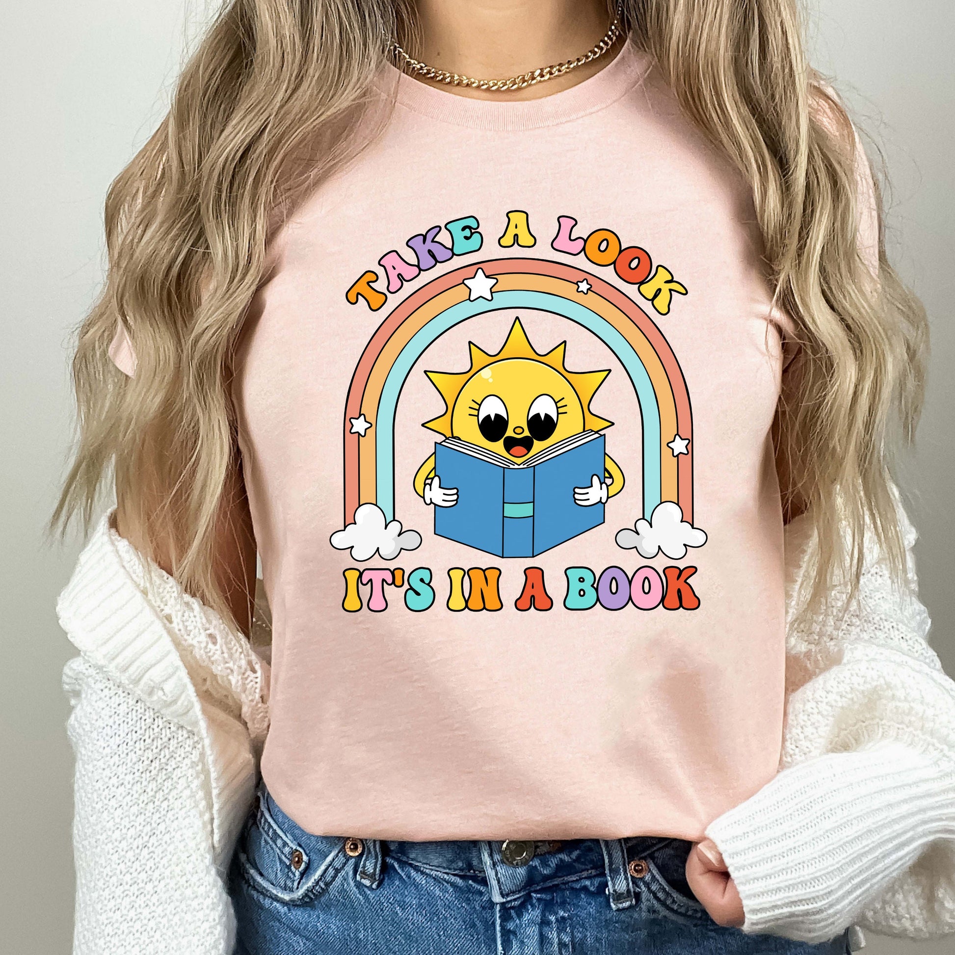 A fun and engaging design featuring a sun reading a book under a rainbow with fluffy clouds The phrase take a look it&#39;s in a book is displayed in vibrant letters capturing a sense of wonder and learning