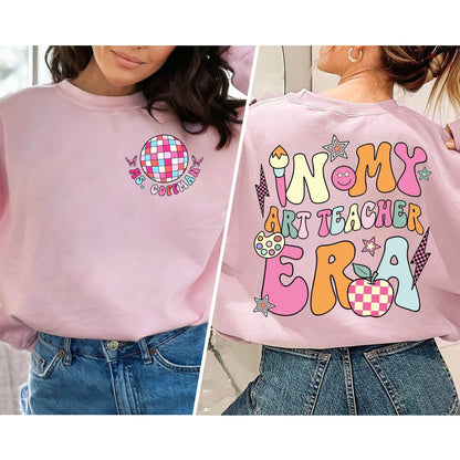 A playful homage to art educators, the illustration displays IN MY ART TEACHER ERA in an array of bright, pastel colors, adorned with whimsical doodles including a cheerful paint palette, a large paintbrush, and a stylized apple,