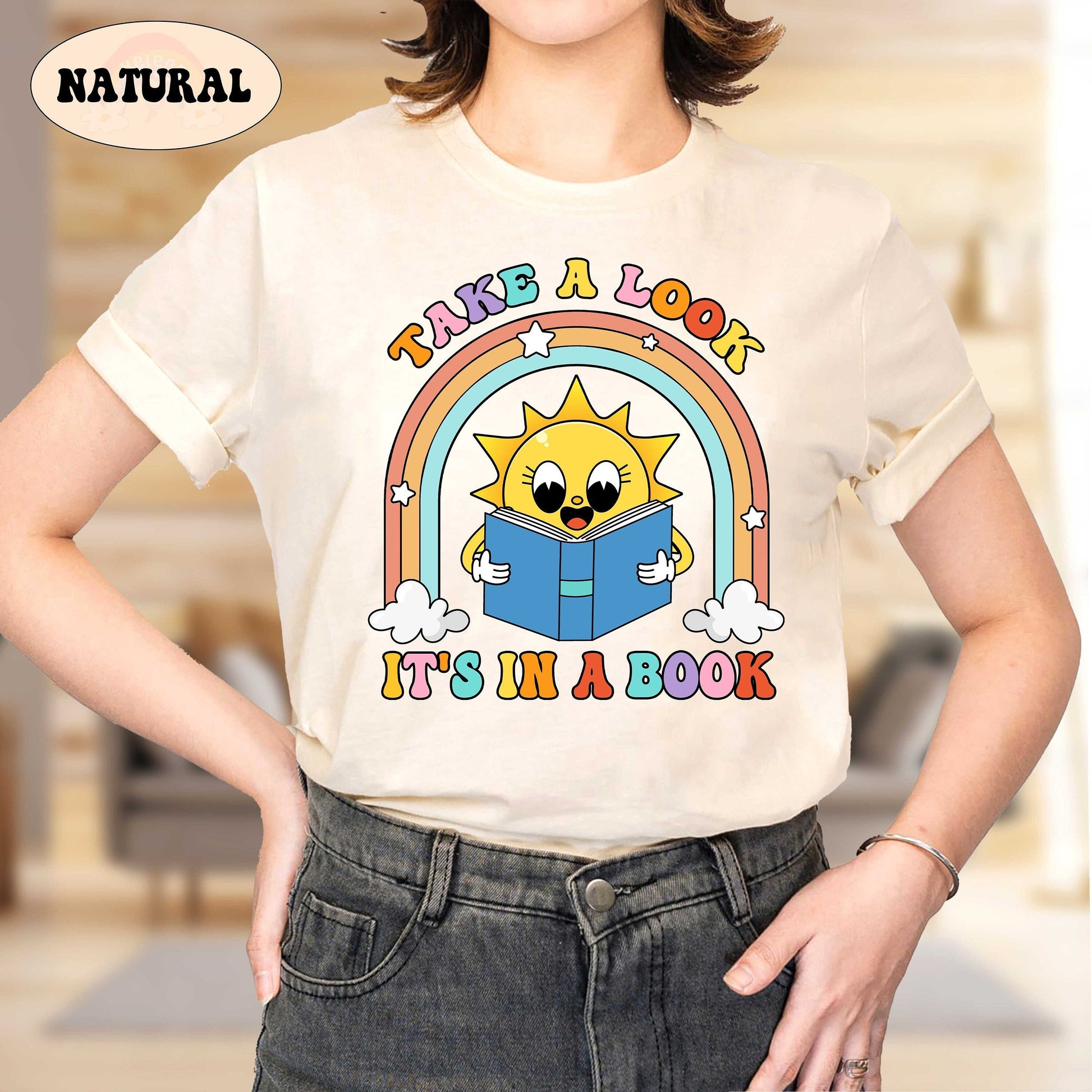 A cheerful design featuring a smiling sun holding an open book with a colorful rainbow arching above The text take a look it&#39;s in a book is displayed in playful fonts adding a fun and inviting vibe