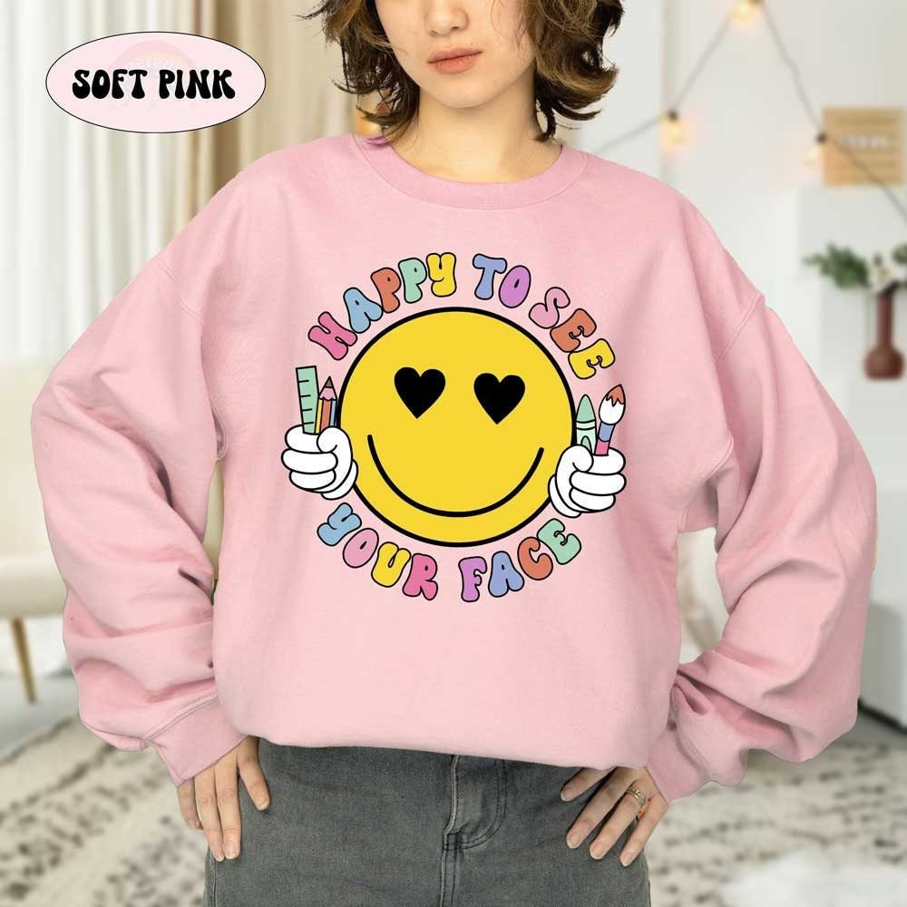 A radiant yellow smiley face holds school supplies, framed by the colorful message HAPPY TO SEE YOUR FACE in a friendly and welcoming design.