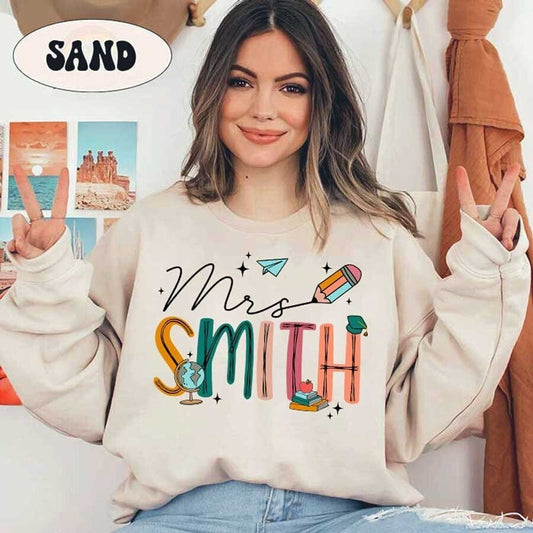 A creative design featuring Mrs. Smith with letters made from school-themed elements like a globe, books, and a pencil plus accents like a paper airplane and cap.