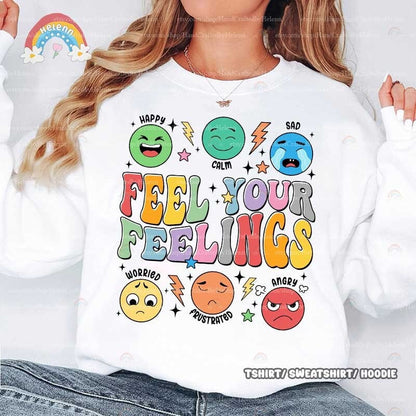 A lively and supportive design that depicts the phrase FEEL YOUR FEELINGS, illustrated in soft pastel hues, encircled by a variety of emoticons displaying different feelings, highlighted with whimsical star and lightning bolt shapes.