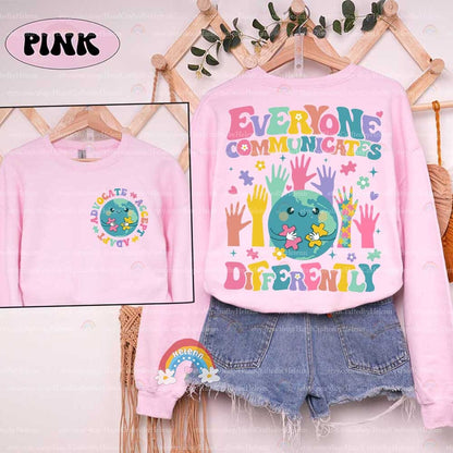 The illustration encapsulates the beauty of diverse interactions with a central globe character piecing together puzzles, encircled by a variety of vibrant hands reaching in, all beneath the guiding words EVERYONE COMMUNICATES DIFFERENTLY