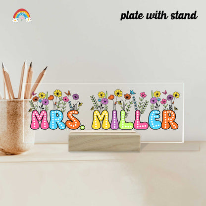 This artistic rendition presents MRS. MILLER in bold, polka-dotted letters, each in a different hue. The background is adorned with an array of spring flowers and butterflies, symbolizing growth and transformation.