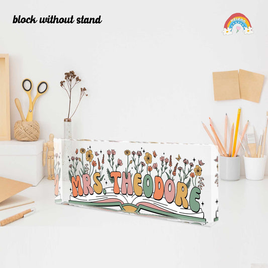The image features a stylish desk nameplate for Mrs. Theodore, displayed on a wooden stand, adorned with an array of beautifully illustrated flowers sprouting from an open book.