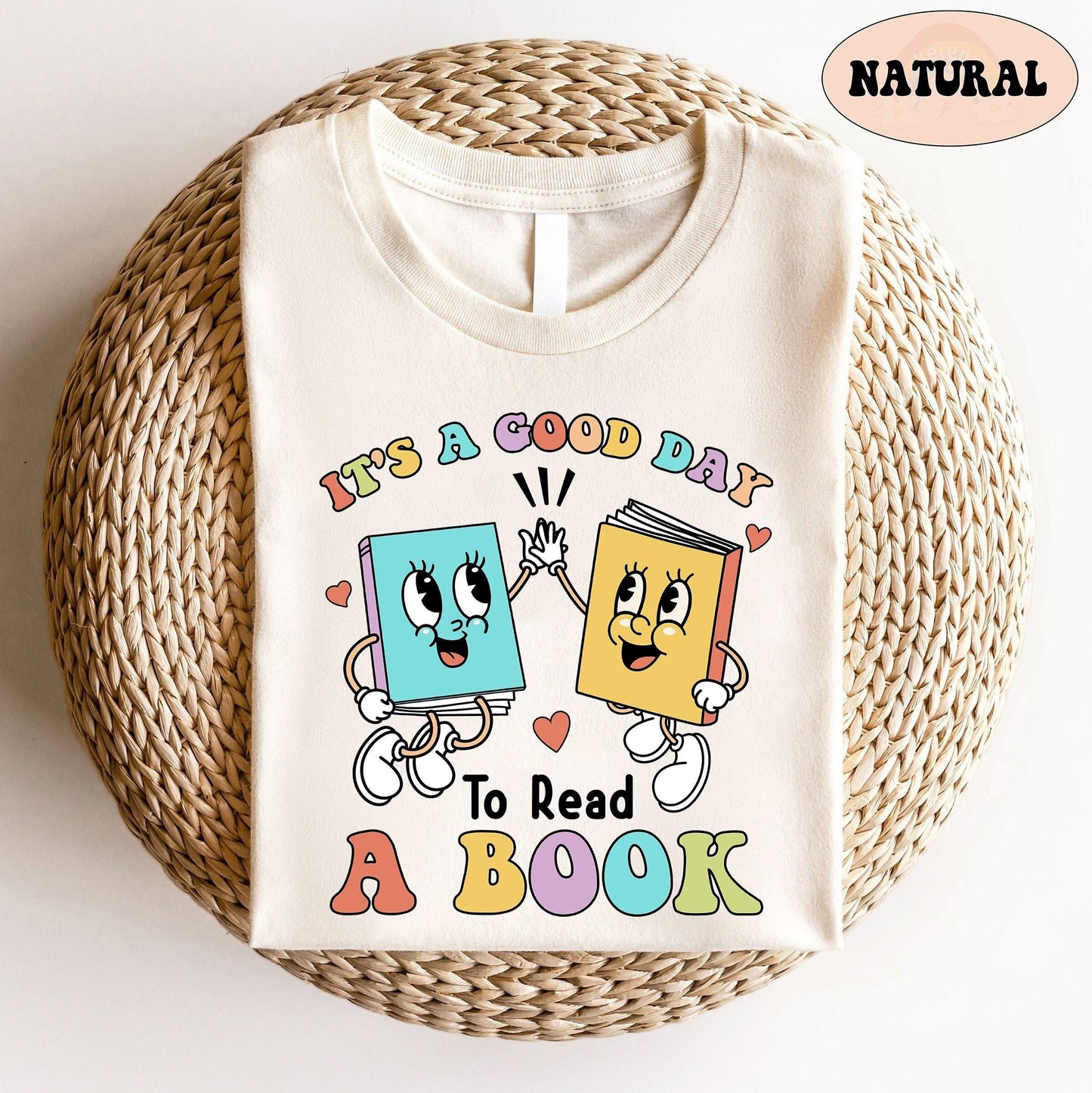 The joyful scene depicts two anthropomorphic books, each with lively expressions and cartoonish limbs, high-fiving over the encouraging words IT&#39;S A GOOD DAY TO READ A BOOK displayed in a playful font with an array of pastel colors.