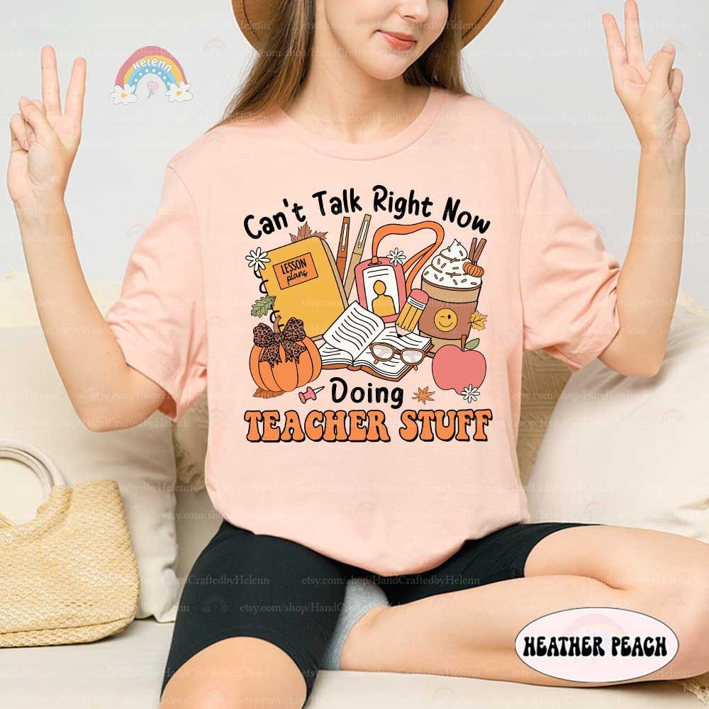 This design showcases a cozy fall aesthetic with elements like a pumpkin, hot beverage, and classroom supplies, perfect for teachers celebrating the season.