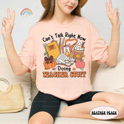 This design showcases a cozy fall aesthetic with elements like a pumpkin, hot beverage, and classroom supplies, perfect for teachers celebrating the season.