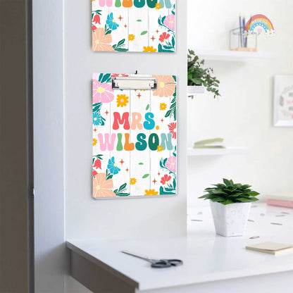 The clipboard showcases a personalized touch with Mrs. Wilson written in colorful, bold letters surrounded by a variety of bright flowers.
