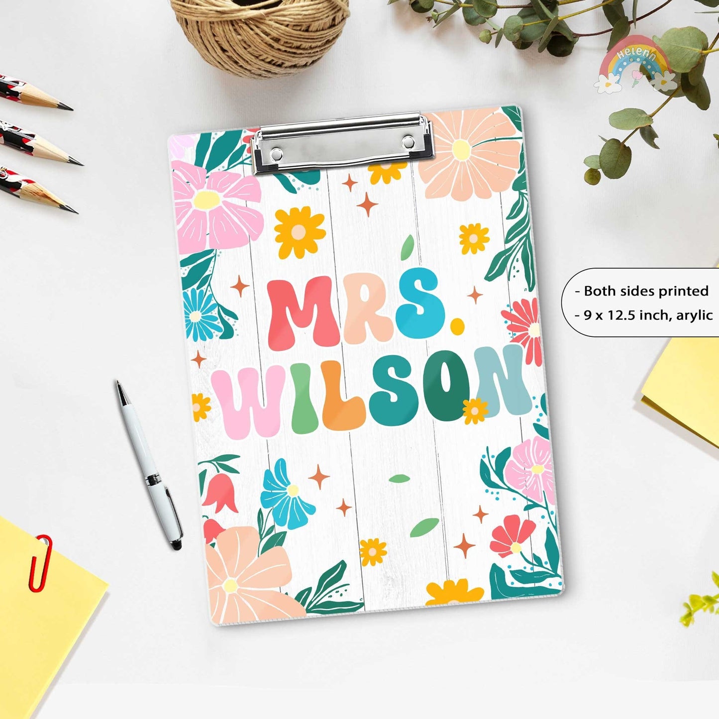 A vibrant and colorful clipboard featuring the name Mrs. Wilson set against a white wooden background adorned with floral patterns.