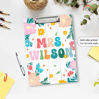 A vibrant and colorful clipboard featuring the name Mrs. Wilson set against a white wooden background adorned with floral patterns.