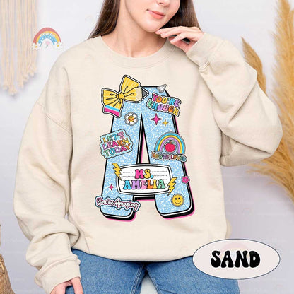 A bright and fun design with large letters representing different colors decorated with cheerful icons like bows and smiley faces Each letter includes the teacher&#39;s name in a playful font