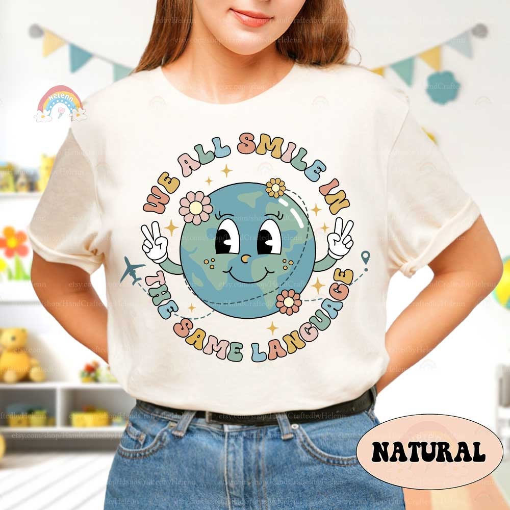 A vibrant design featuring the phrase We all smile in the same language around a globe character giving peace signs The design includes floral elements and an airplane emphasizing global unity and happiness