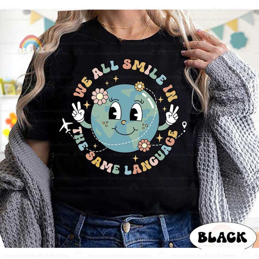 A cheerful design featuring a smiling globe holding up peace signs surrounded by the phrase We all smile in the same language The design is accented with flowers and a small airplane creating a message of unity and positivity