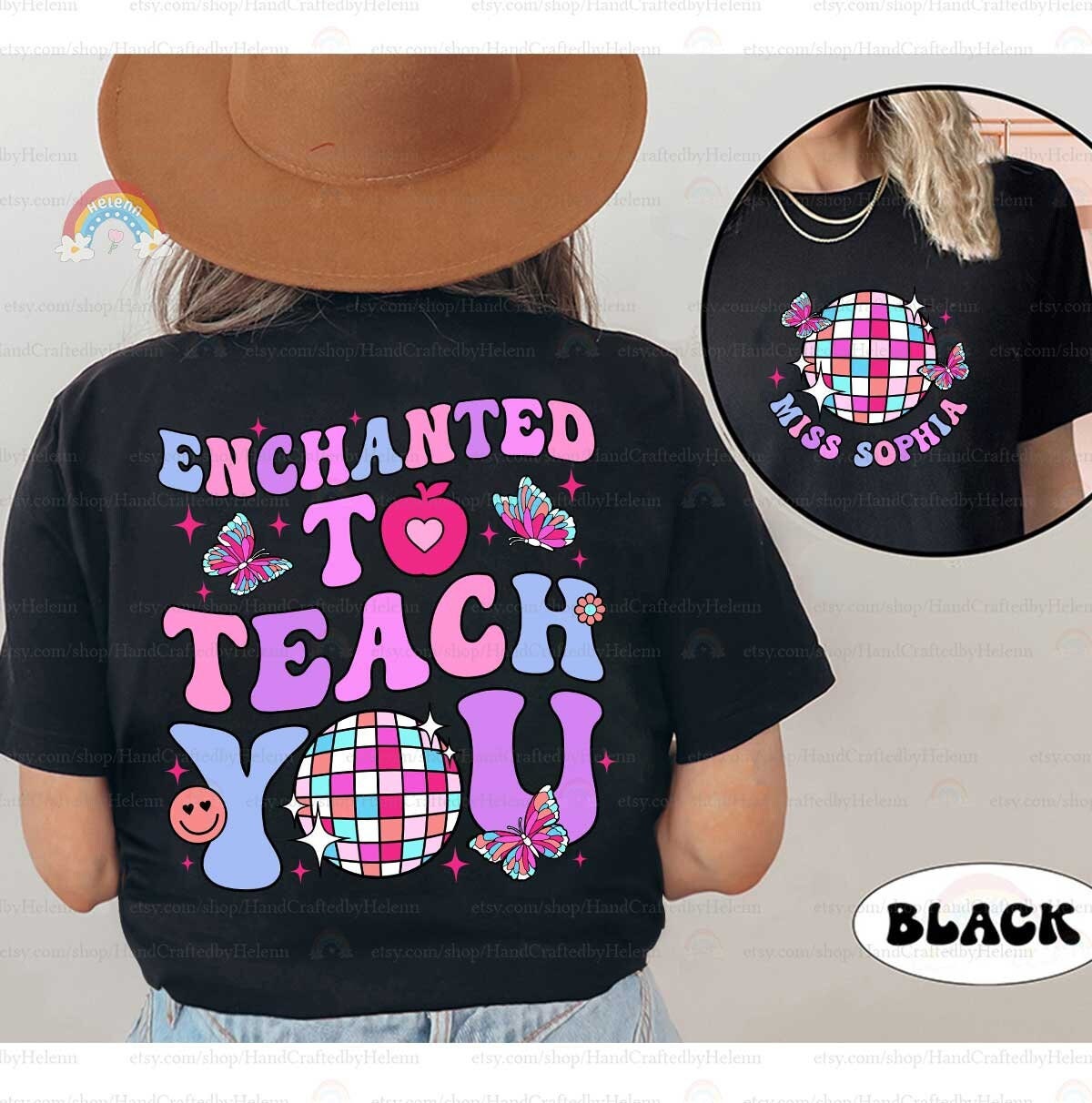 A playful shirt design featuring the phrase Enchanted to Teach You in bold, colorful letters with accents like butterflies, a heart-shaped apple, and a checkered disco ball.