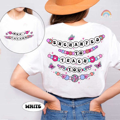 This T-shirt showcases a magical theme with the phrase Enchanted to Teach You, creatively arranged with beaded letters, butterflies, and hearts. The custom name on the front adds a unique, personal element to this enchanting design.