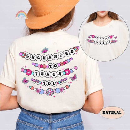 Enchanted and playful T-shirt design with beaded text reading Enchanted to Teach You, decorated with butterflies, hearts, and cheerful accents. The personalized name on the front makes it a perfect choice for teachers.