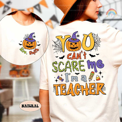 A playful Halloween design featuring the phrase You can&#39;t scare me I&#39;m a teacher in bold colorful letters The design includes fun Halloween elements like a jack-o&#39;-lantern with a witch hat spider webs bats a pencil and candy corn