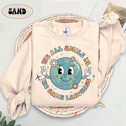 A fun and positive graphic with a smiling globe holding peace signs and the phrase We all smile in the same language The design is enhanced with flowers and a small airplane symbolizing global peace and connection