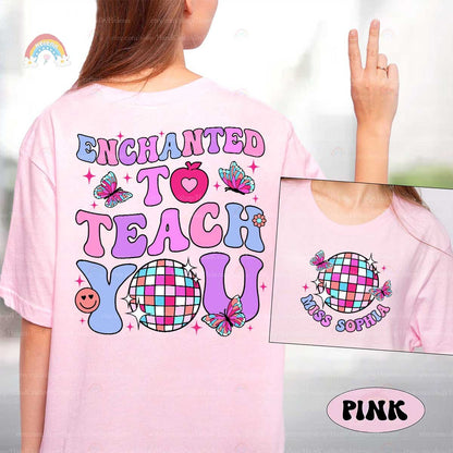 A cheerful shirt design featuring Enchanted to Teach You in bright letters, accented with butterflies, a heart apple, and a checkered disco ball, adding a fun and enchanting touch.