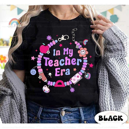 Charming and playful T-shirt design featuring the phrase In My Teacher Era, encircled by a beaded bracelet with cute charms like apples, flowers, and smiley faces. A fun and stylish way to celebrate being a teacher.