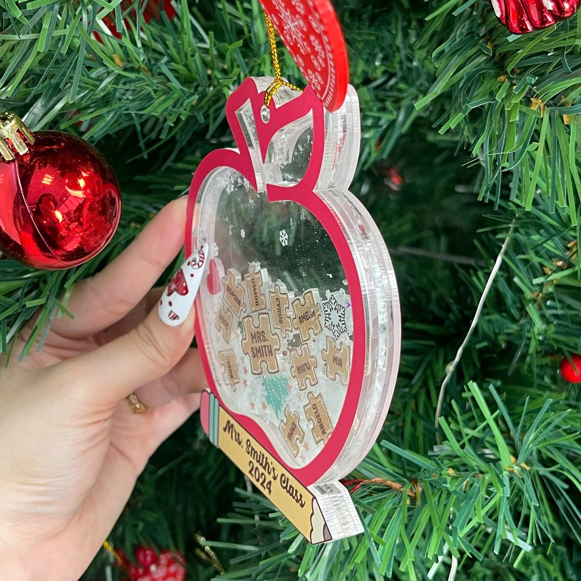 This charming teacher ornament is designed as a red apple with personalized puzzle pieces displaying student names, centered around Mrs. Smith. The shakeable snow and festive details make it a perfect gift for the holidays.