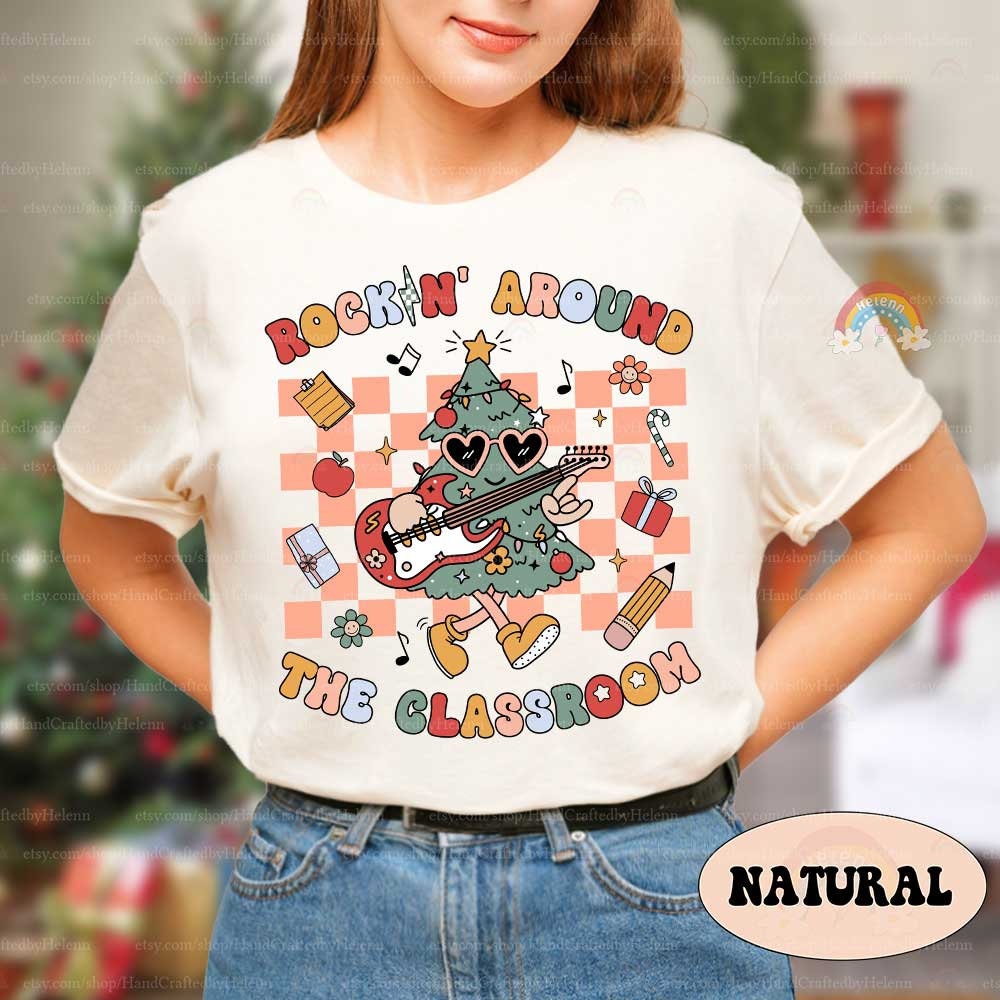 Playful and colorful T-shirt design with a Christmas tree rocking an electric guitar, decorated with festive and classroom accents like gifts, pencils, and notes. The phrase Rockin&#39; Around the Classroom brings a fun holiday spirit to school.