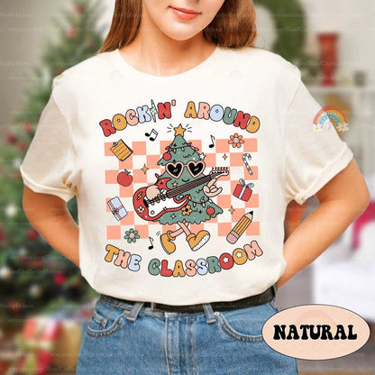Playful and colorful T-shirt design with a Christmas tree rocking an electric guitar, decorated with festive and classroom accents like gifts, pencils, and notes. The phrase Rockin&#39; Around the Classroom brings a fun holiday spirit to school.