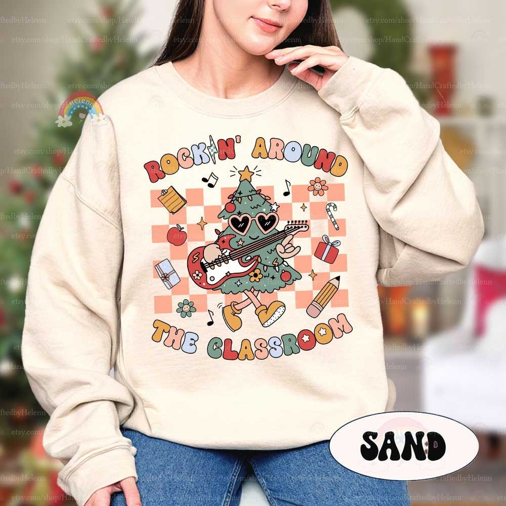 Festive and fun T-shirt design featuring a cool Christmas tree wearing sunglasses and playing an electric guitar, surrounded by classroom-themed items like books, pencils, and gifts. The phrase Rockin&#39; Around the Classroom adds a playful twist.