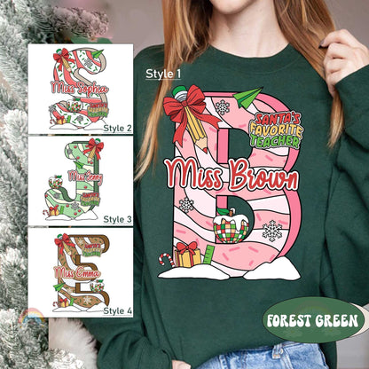 Playful and bright T-shirt design featuring a customized letter filled with Christmas decorations, from bells to wrapped gifts. The addition of the teacher&#39;s name, like Miss Brown, creates a fun and personalized holiday look.