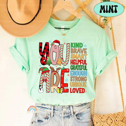 Colorful and playful T-shirt design with holiday-themed letters and a list of positive qualities such as Helpful, Grateful, and Strong. This cheerful design encourages positivity during the holiday season.