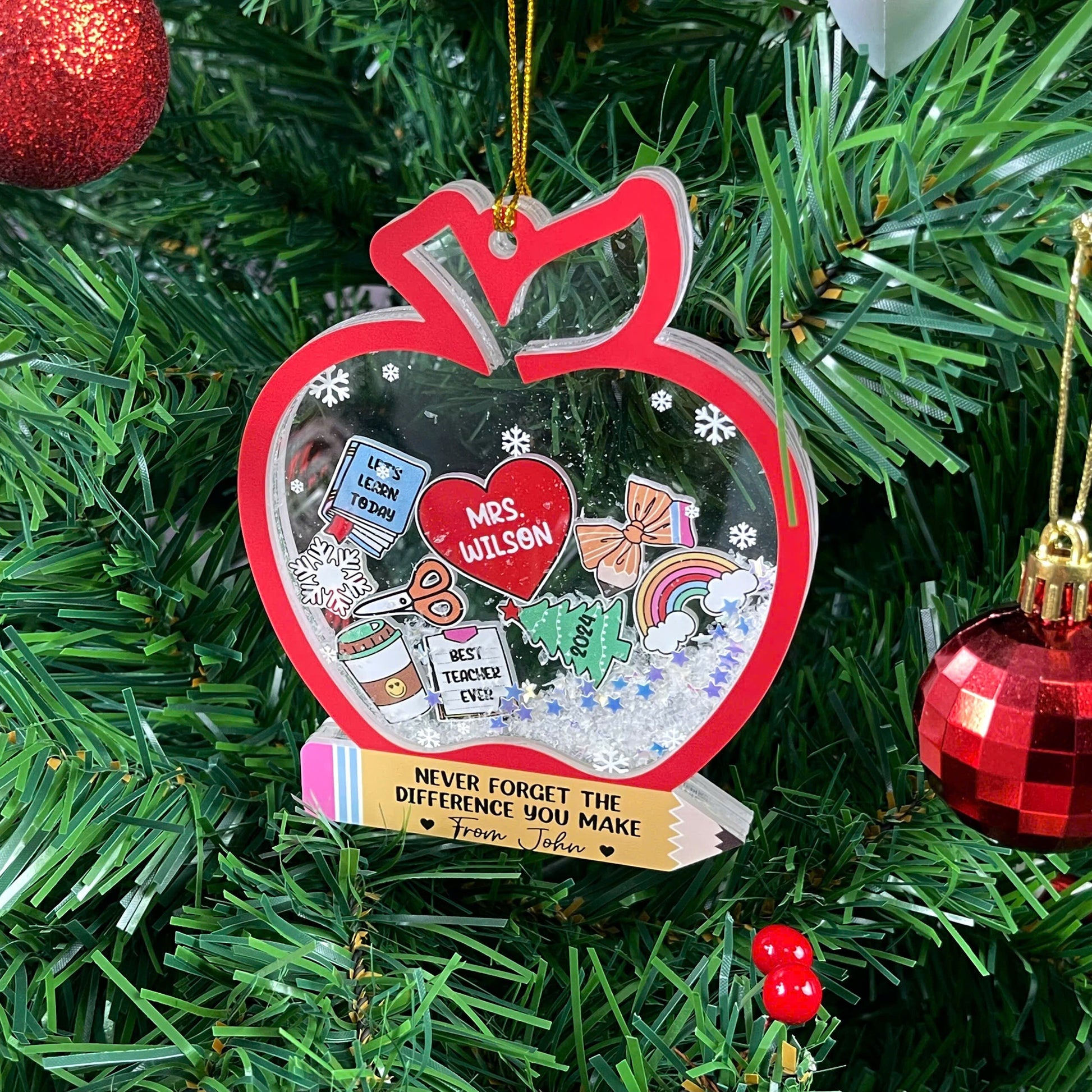 Whimsical apple-shaped ornament filled with personalized items for Mrs. Wilson, including a book, scissors, and a coffee cup, all surrounded by snowflakes. The heartfelt message from John adds a special touch to this festive teacher gift.