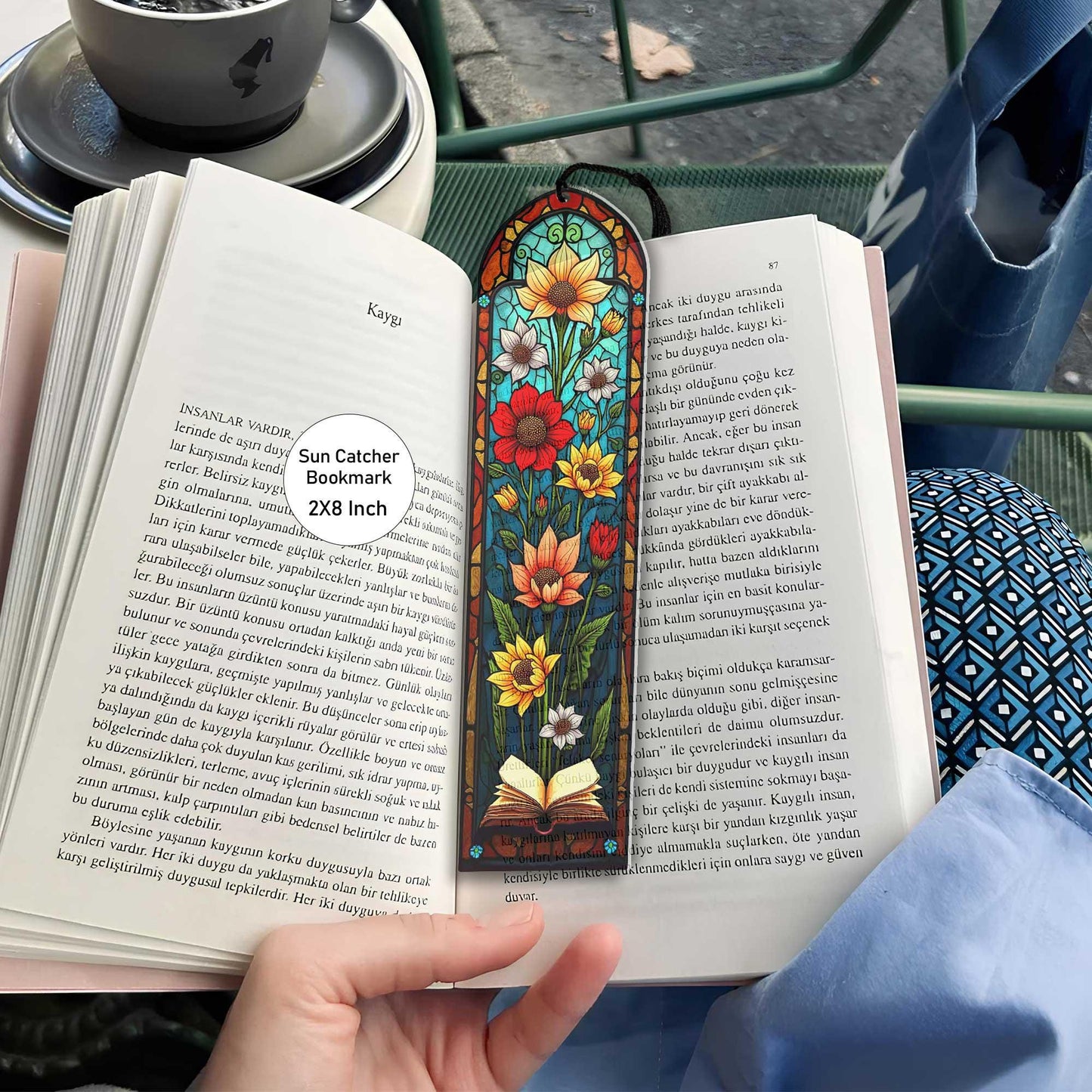 May include: A stained glass bookmark with a floral design. The bookmark features sunflowers, red flowers, and a book with a blue background. The bookmark is 2x8 inches and is called a Sun Catcher Bookmark.