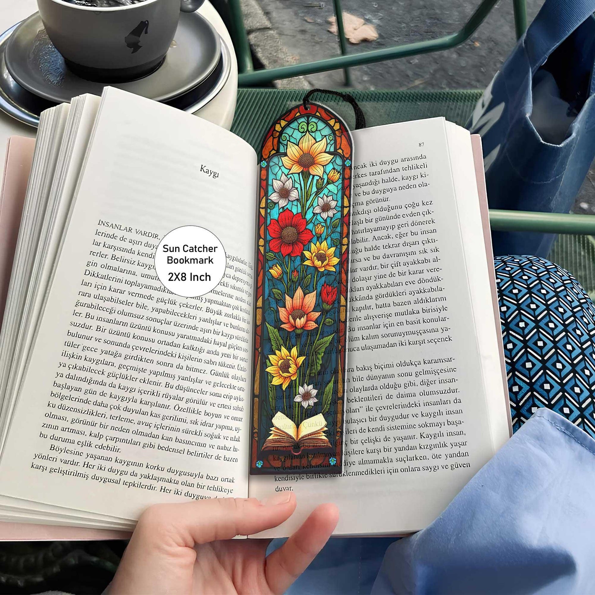 May include: A stained glass bookmark with a floral design. The bookmark features sunflowers, red flowers, and a book with a blue background. The bookmark is 2x8 inches and is called a Sun Catcher Bookmark.