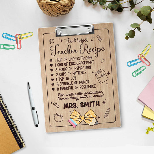 May include: Wooden teacher appreciation clipboard with engraved recipe for a perfect teacher.  The recipe includes ingredients such as understanding, encouragement, inspiration, patience, joy, humor, and resilience.  The clipboard features a cute illustrated bow and the name &#39;MRS. SMITH&#39; is personalized at the bottom. The clipboard is light brown with dark brown engraved text and illustrations.