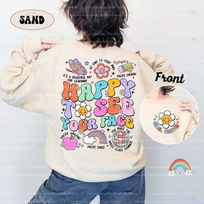 May include: A beige sweatshirt with a colorful graphic print on the back. The graphic includes the words &#39;Happy to see your face&#39;, a rainbow, a flower, a globe, an apple, and a butterfly. The front of the sweatshirt has a smaller graphic of a flower with a smiley face and the words &#39;Mrs. Smith&#39;.