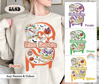 May include: A white sweatshirt with a graphic design of a dripping orange number 2 with various Halloween themed images including a ghost, a witch&#39;s hat, a pumpkin, and a disco ball. The text &#39;Miss Sophia&#39; is written in black and the text &#39;trick or teach&#39; is written in black and white. The sweatshirt is shown in four different colors: orange, purple, green, and yellow.